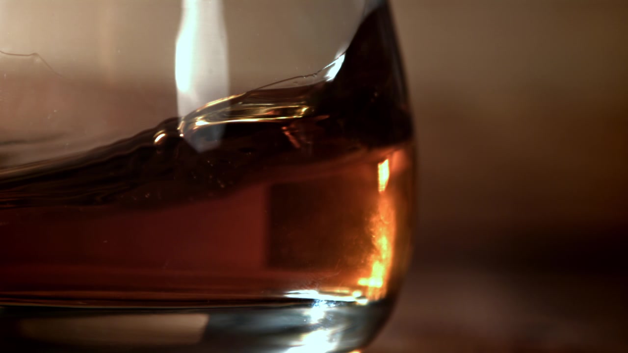 Primo piano di whisky ambrato che vortica in un bicchiere al rallentatore