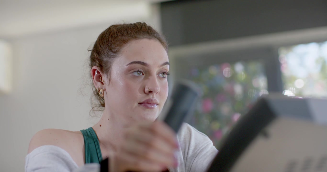 Woman gripping bike handles starting at home, checking console and wrist tracker to monitor pulse