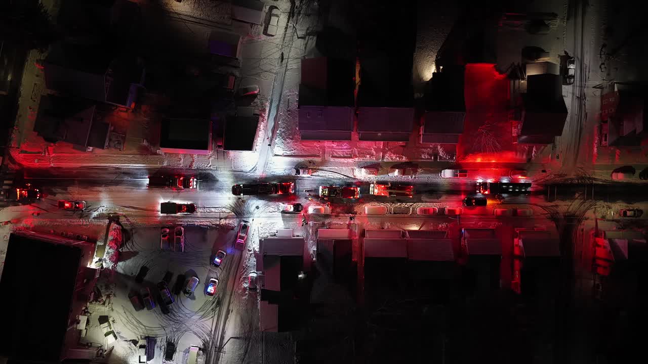 Firefighters and emergency vehicles helping on snow-covered residential street, with flashing red lights illuminating winter conditions in American neighborhood. Aerial top down shot. Emergency stop