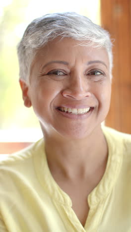 vertical video of portrait of happy senior biracial woman with short hair at home, slow motion