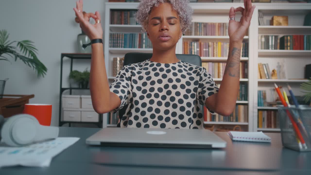 Young african american woman closes laptop and meditates sits at office desk