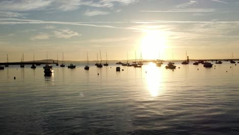 boats silhouetted on golden shimmering harbour ocean surface low aerial view