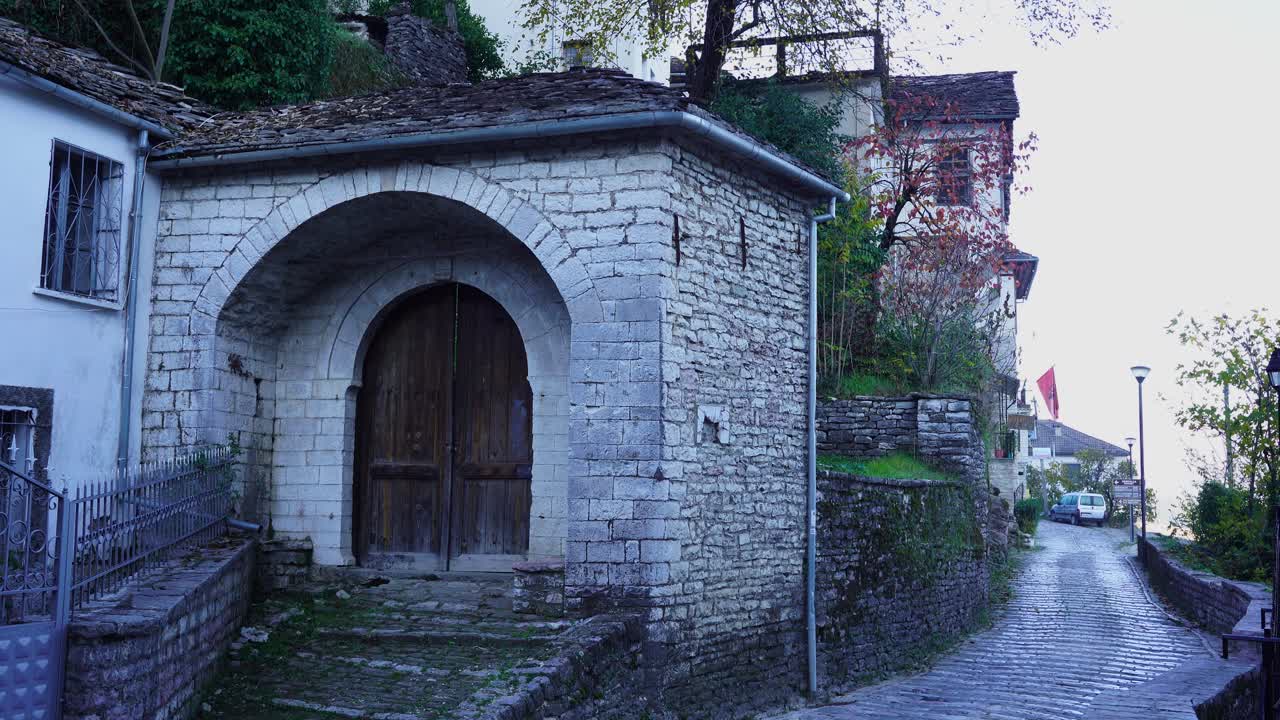 antigua puerta de casa con paredes arqueadas de piedra y callejón pavimentado en gjirokastra, albania