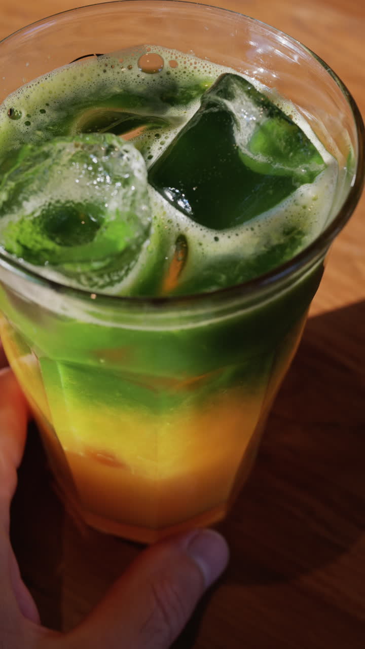 Close up of a glass of an iced orange juice matcha on a table at a cafe. Vertical