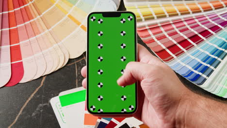 mano sosteniendo un teléfono inteligente con una pantalla verde, rodeado de muestras de color.