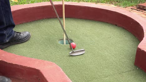 jogador encaçapando a bola no green do campo de minigolfe