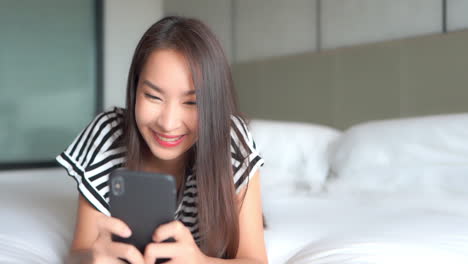 close-up of a young attractive woman texting on her smartphone while lying on a big comfy bed