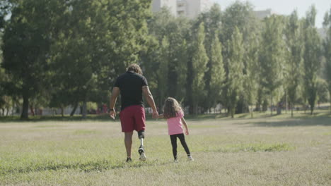 Back-view-of-dad-with-disability-and-daughter-walking-in-park