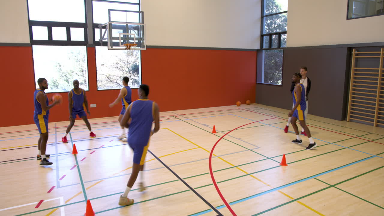 Jogadores de basquete praticando exercícios no ginásio com o treinador observando atentamente