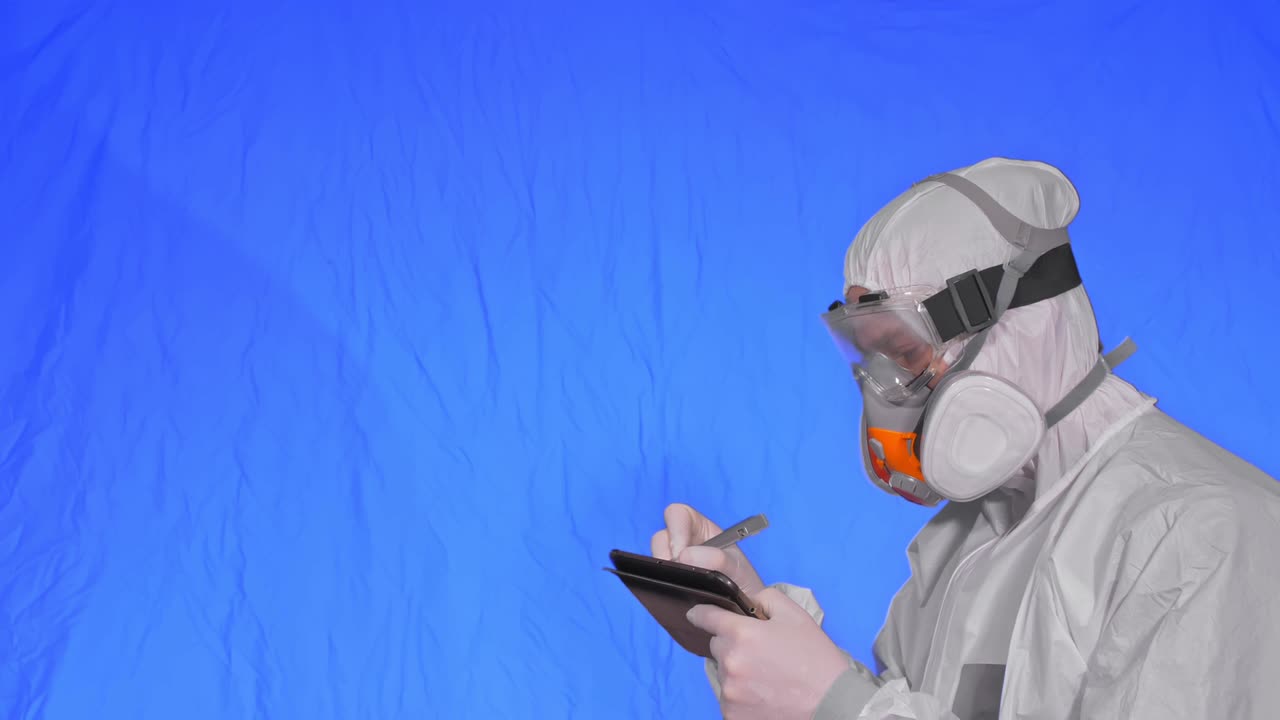 científico virólogo en respirador hace escribir en una tableta con lápiz. hombre con máscara médica protectora. clave de croma azul