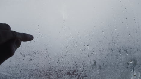 Close-up-of-a-finger-tracing-the-word-"Love"-on-a-foggy-window,-creating-a-heartfelt-message