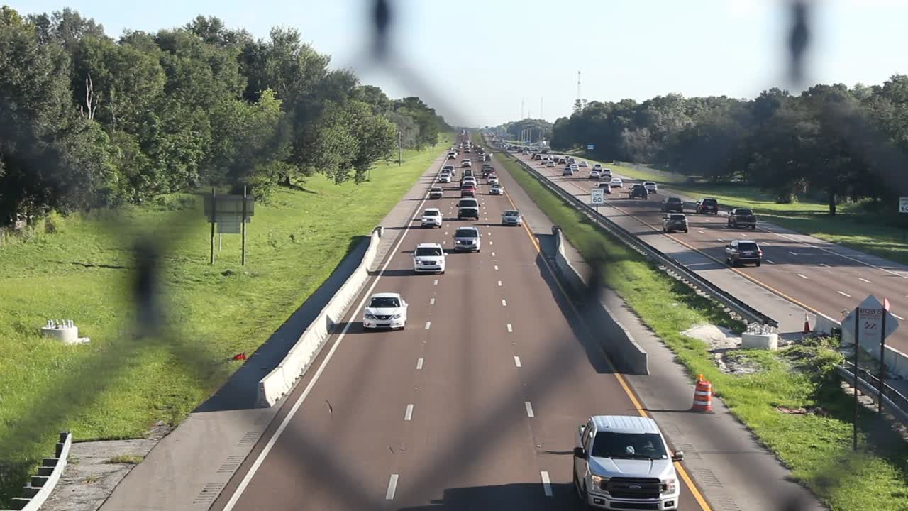 Cars speed down highway, still shot, day, through fence on overpass, sped up timelapse.