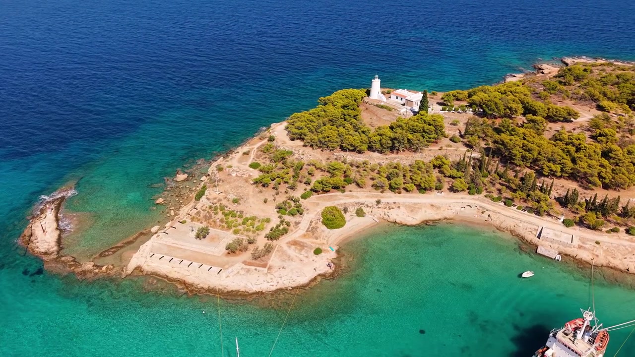 La icónica península del faro de Spetses se extiende hacia brillantes aguas turquesas, rodeada de un bosque de pinos y costas rocosas. Una histórica batería de cañones y un sendero costero serpentean alrededor de este pintoresco promontorio
