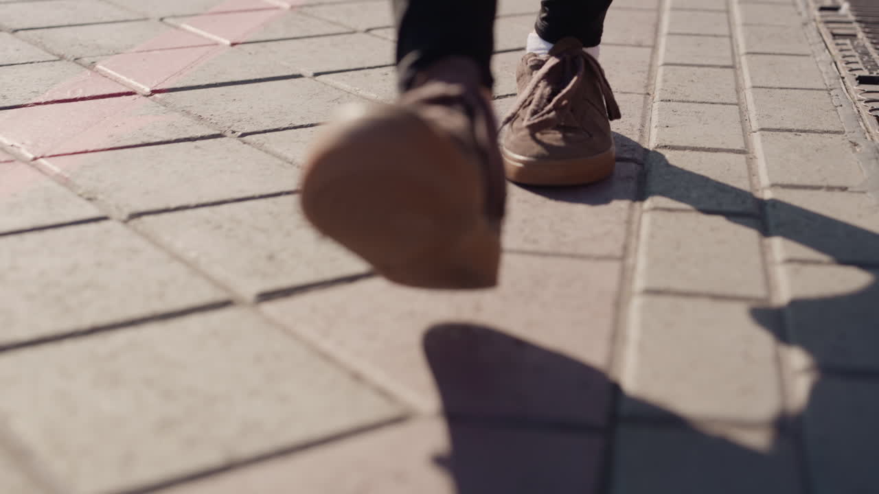 Avanzando dolcemente. Camminando silenziosamente sul marciapiede. Una persona procede in silenzio su un sentiero illuminato dal sole. Un individuo solitario cammina tranquillamente lungo un marciapiede texturizzato proiettando una lunga ombra.