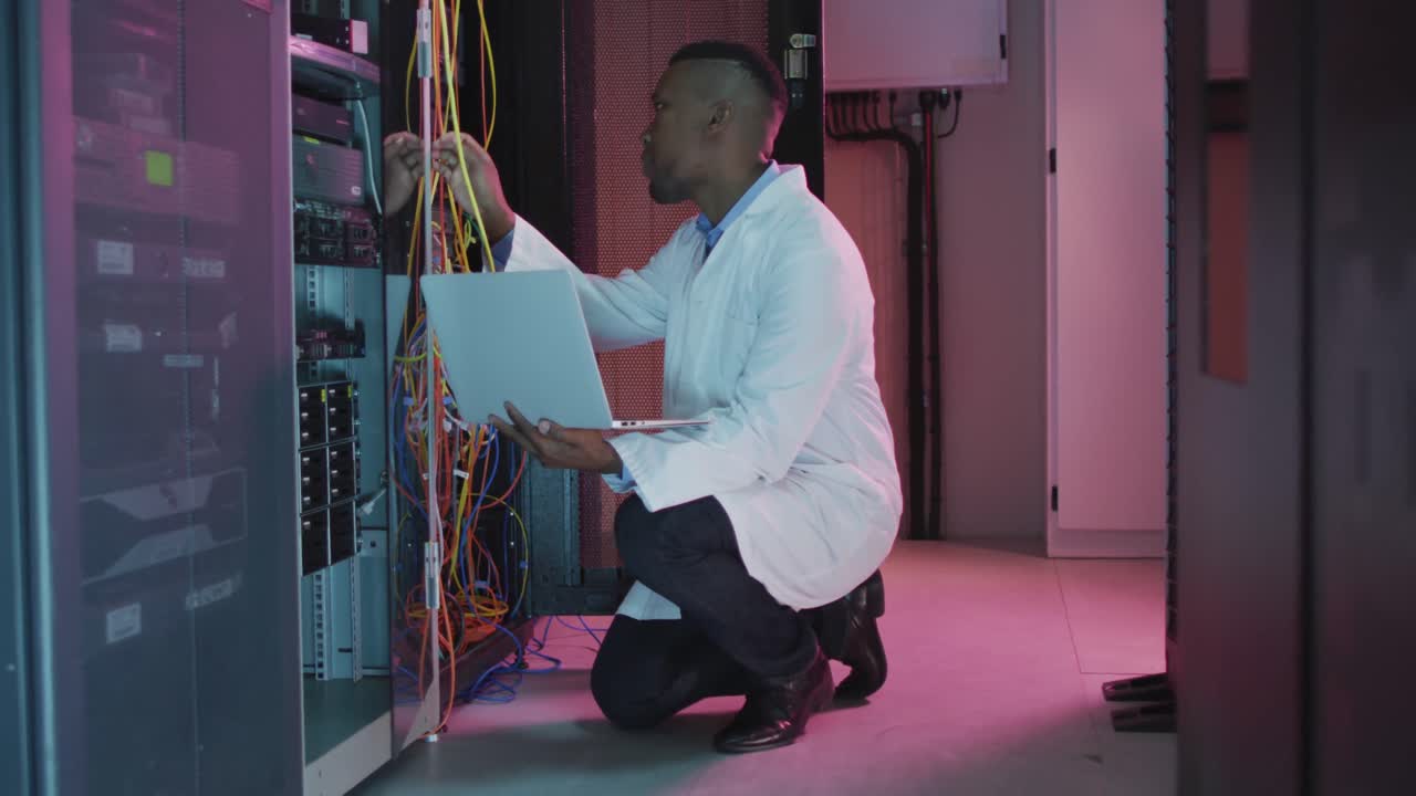 African american male computer technician using laptop working in business server room