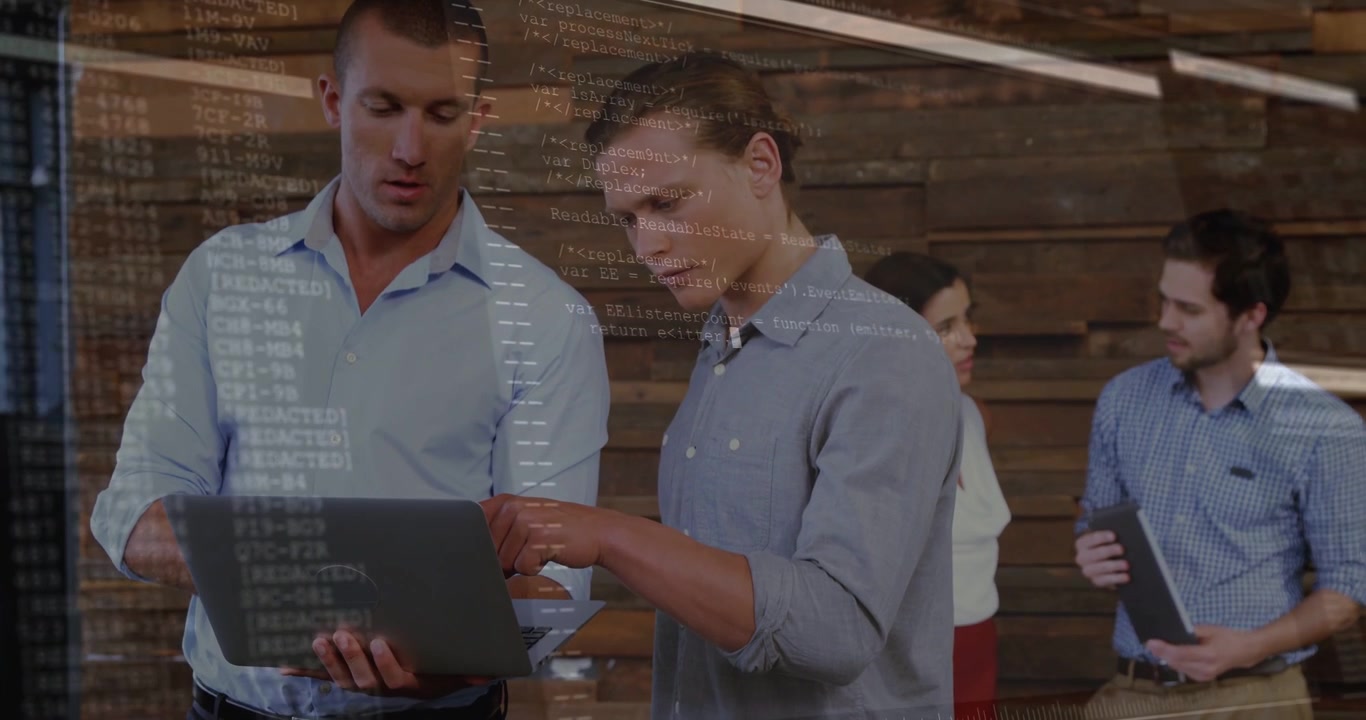 Two men holding laptop and pointing screen, creating code overlay while dev team reviewing plans
