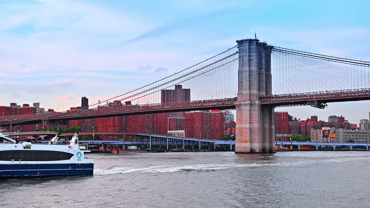 White and blue riverboat moving slowly by the waterscape of the East River. Low angle view at the Brooklyn Bridge in New York, USA