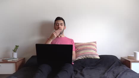 hombre acostado en la cama, saludando a la pantalla de su computadora portátil y lanzando besos