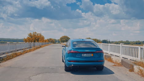 futuristic electric car. blue automobile driving on an empty road. luxury audi moving on bridge in the countryside. back view.