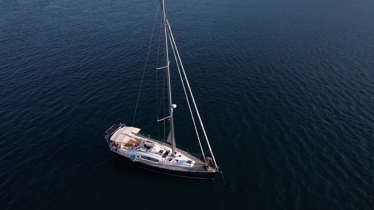 Volo sopra una barca a vela e acque marine di un blu profondo, vista aerea con drone