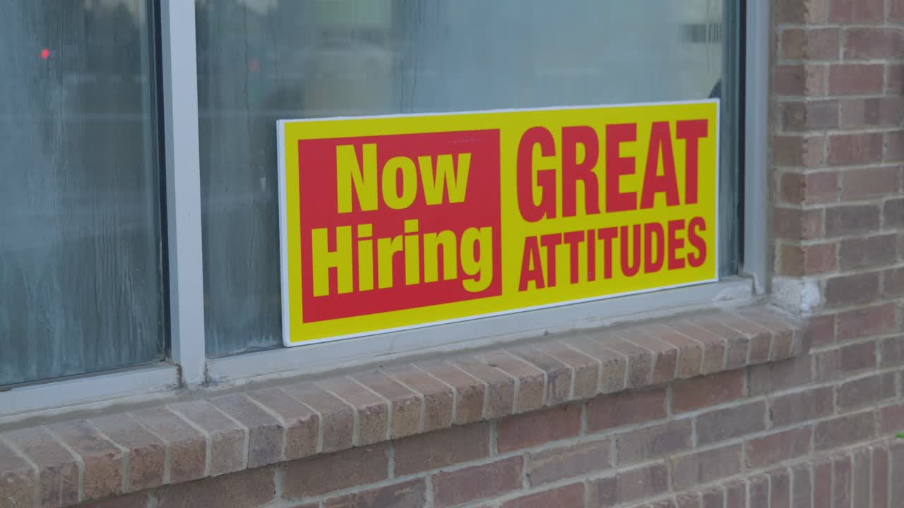 Now hiring great attitudes bright yellow and red sign in window of car wash with condensation dew on glass and brick wall slight movement from camera in Cinema 4K 30fps slowed from 60fps