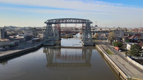 4K-aerial-static-shot-of-Puente-Transbordador-Nicolas-Avellaneda-bridge-with-its-reflection-on-Riachuelo-Matanza-river-and-traffics-motions-in-the-background,-Buenos-Aires,-Argentina