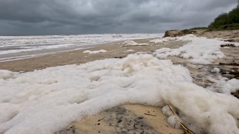 una escena de playa tormentosa con espuma marina que se lava en tierra, bajo cielos nublados, capturando la interacción dinámica de las olas y la arena