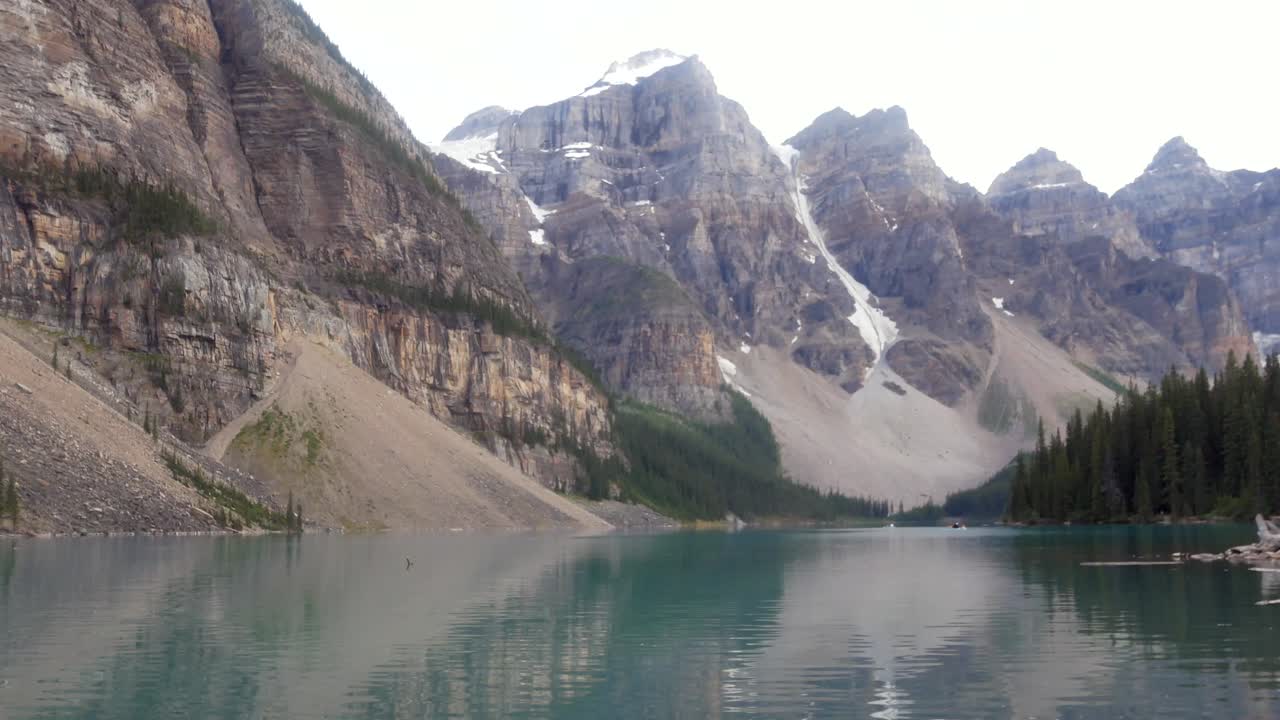 vista del paisaje en el lago moraine con gente en canoa en la superficie del lago espejo verde y la cordillera de las montañas rocosas durante el día de verano