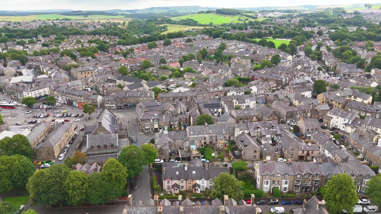Aerial footage glides over a traditional English town with stone buildings, tree-lined streets, and rolling countryside under soft daylight, captured in a smooth ascending motion