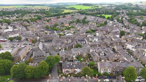 aerial footage glides over a traditional english town with stone buildings, tree-lined streets, and rolling countryside under soft daylight, captured in a smooth ascending motion