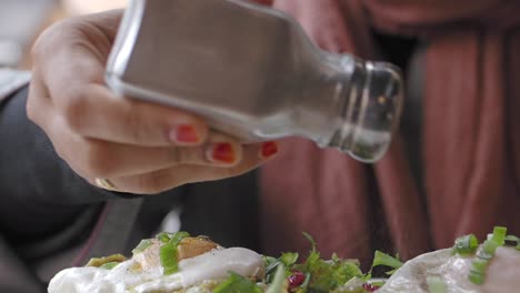 person seasoning a meal with a salt shaker