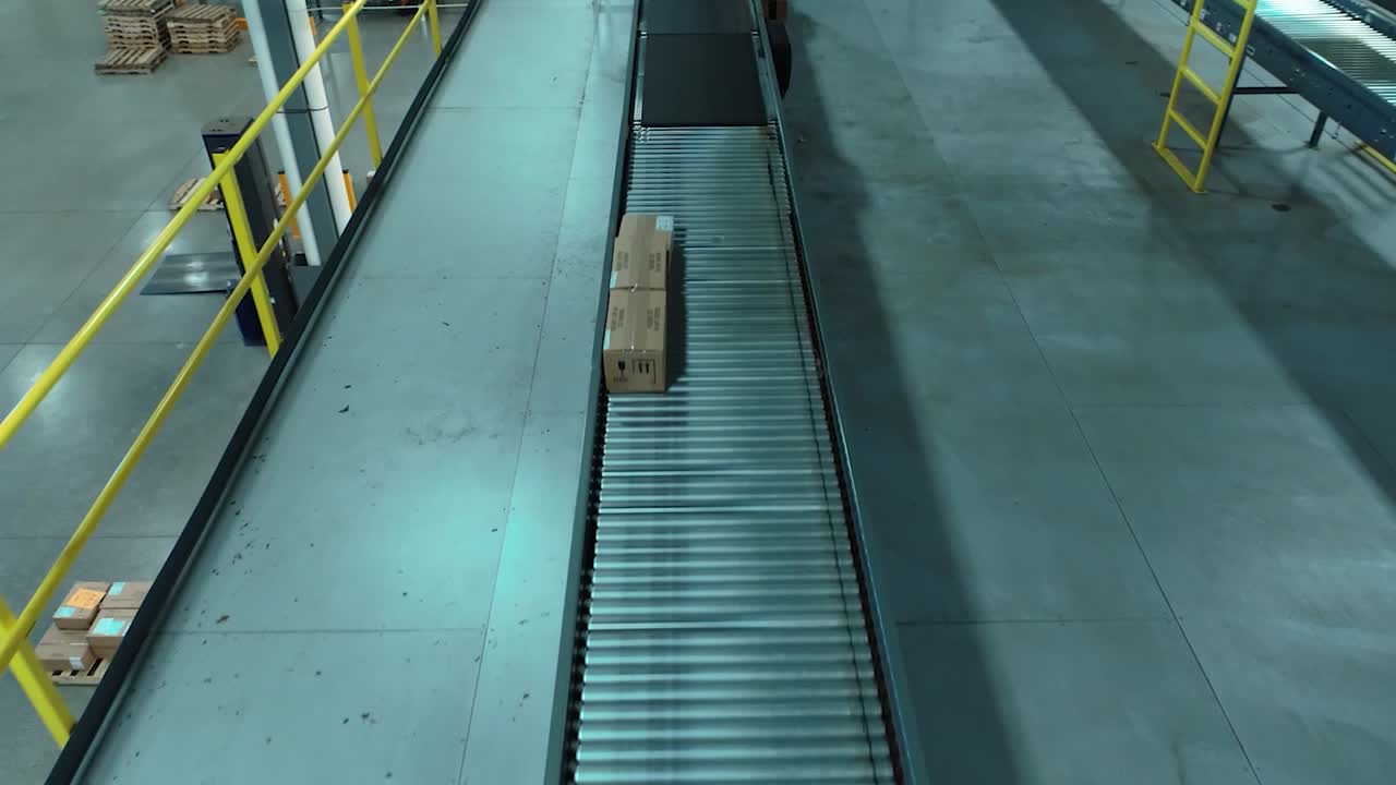 A forward-moving drone shot gliding over elevated conveyor belts and spiral slides that transport boxes across a large warehouse
