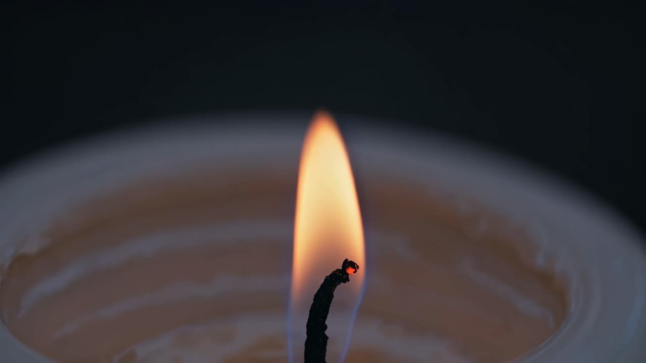 Detailní video plamene svíčky, zachycené z nízkého úhlu. Jemná záře a teplé barvy