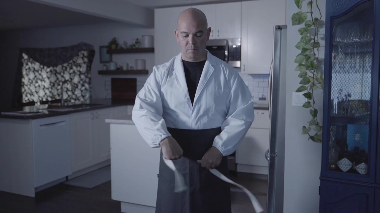 Eine statische Frontalaufnahme eines Kochs, der eine Schürze anzieht und zum Spülbecken geht, wobei die Küchenvorbereitung und die Bedeutung der Hygiene vor dem Kochen betont werden. Perfekt für kulinarische Inhalte