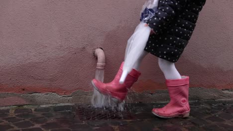 girl in pink boots plays on the water from the house drain pipeline. - close up