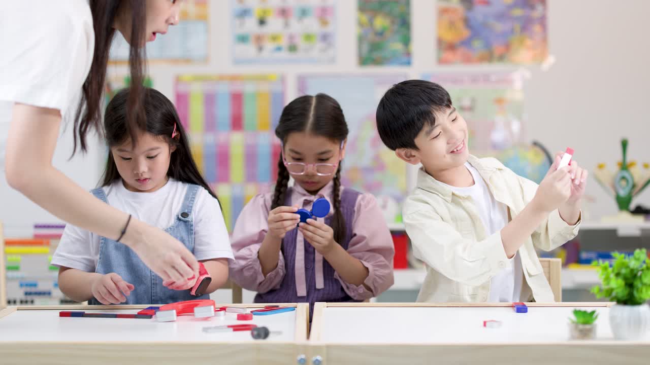明るい教室で、小学生3人が先生の指導のもと、カラフルな磁石を使った理科の授業を受けている様子。