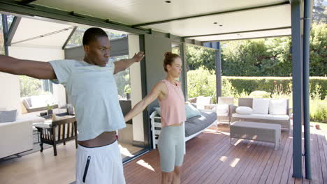 diverse couple practicing yoga on wooden deck, at home