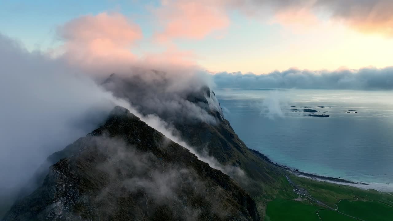 Fog wraps Mannen peaks as ocean fog climbs over mountains and Utakleiv glows in pink midnight sun in Lofoten