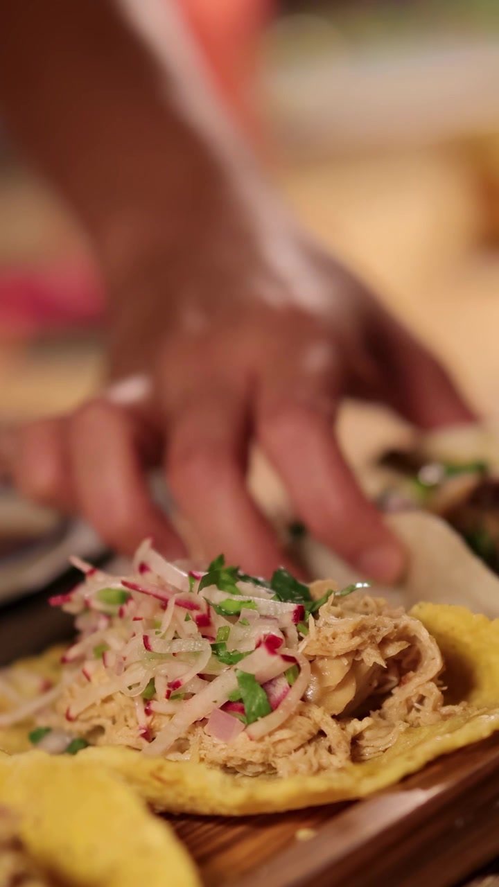 Hænder samler tacos med friske ingredienser i en livlig, farverig restaurantindstilling. Varm belysning forstærker den indbydende atmosfære.