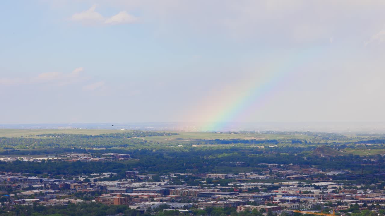 A stunning rainbow arcs gracefully over the town of Boulder, Colorado, following a summer rain shower. The colors pop vividly against the dramatic mountain backdrop.