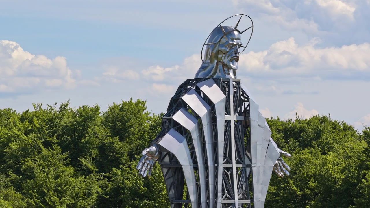Aerial drone view of a steel Christ figure with halo in three-quarter view against a blue sky, Harghita, Transylvania, Romania.
