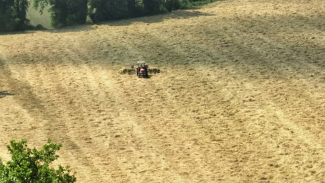 un tractor cosechando un campo dorado bajo el sol, rodeado de árboles verdes en la distancia