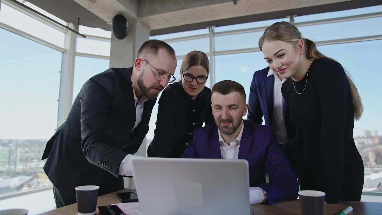 Creative team stand around boss sitting in front of computer. Happy positive young team working on idea in the office. Close up with gradual distancing.