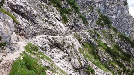 slow left to right pan showing a hiker with orange helmet walking on an exposed alpine german trail with cloudy weather