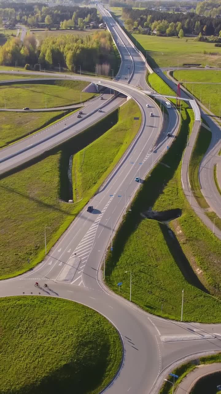 Vertical drone over Katlakalns interchange A5 Riga bypass meets Daugmale road, showing curved ramps, vehicles heading to city center and outskirts, spring fields and forest
