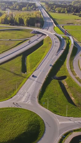 vertical drone over katlakalns interchange a5 riga bypass meets daugmale road, showing curved ramps, vehicles heading to city center and outskirts, spring fields and forest