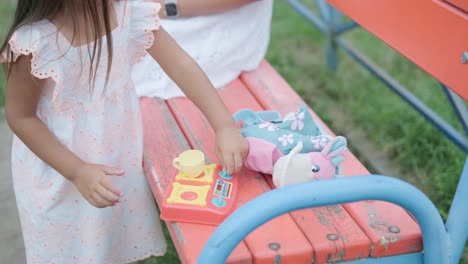 a pregnant mother and her young daughter enjoy playful time together at a playground in the park, surrounded by trees and greenery