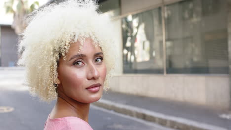 young biracial woman with curly blonde hair gazes thoughtfully with copy space in the city