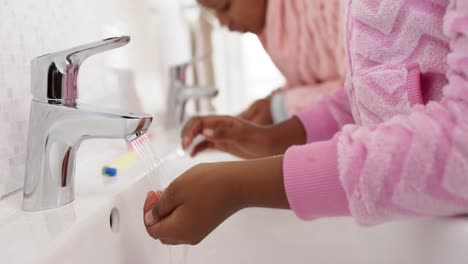 Unaltered-african-american-mother-and-daughter-brushing-teeth-in-bathroom,-in-slow-motion