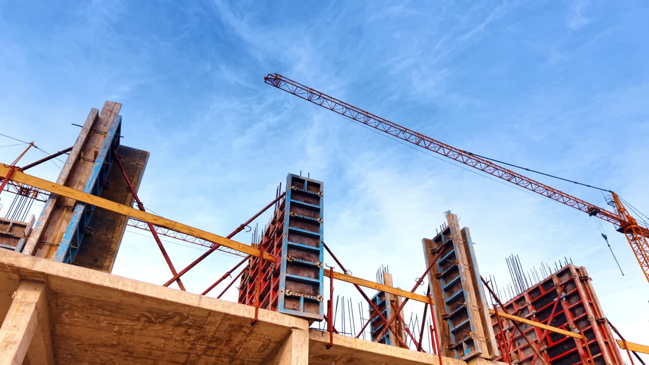 Upper floor of the building under construction from low angle view. Yellow cranes against blue sky at backdrop